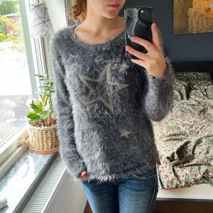 Grå fluffig tröja med stjärnor H&M - Supermjuk och fluffig grå tröja från H&M med stora stickade stjärnor framtill. Tröjan har rund halsringning och långa ärmar, perfekt för kyliga dagar. Den har en lite loose passform och ger en mysig vibe till din outfit.