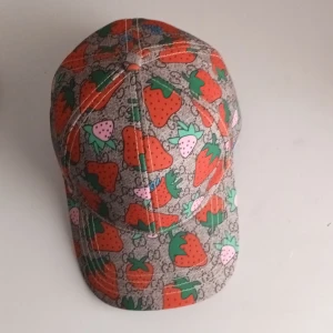 Gucci keps med jordgubbsmönster - Snygg keps från Gucci med färgglatt jordgubbsmönster på beige botten och diskret GG-logga i bakgrunden. Kepsen har justerbar rem i rosa och insida med Gucci-logga. Perfekt för dig som vill sticka ut med en unik accessoar.