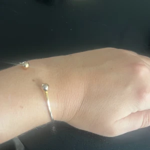 Minimalistiskt armband i silver och guld - Snyggt och stilrent armband med öppen design, dekorerat med två kulor i silver och guld. Perfekt för dig som gillar enkel och modern stil. Armbandet är tunt och passar till alla outfits.