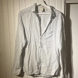 Randig skjorta från H&M i bomull och linne - Säljer en vit skjorta med tunna blå ränder från H&M. Perfekt för en clean och avslappnad look.