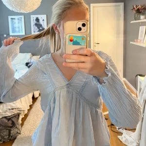 Ljusblå blus från Gina Tricot - Supersöt ljusblå blus från Gina Young med v-ringning och långa ärmar. Blusen har volang nertill och fina spetsdetaljer längs sömmarna. Den är använd ett fåtal gånger men har ändå fått fläckar under armarna( dock syns det inte när den sitter på) därav priset!💕