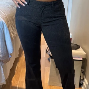 Svarta bootcut kostymbyxor Express - Snygga svarta kostymbyxor från Express med bootcut passform. Byxorna har  mellan låg midja, bälteshällor och dragkedja. Materialet är mjukt och har en lätt stretch för extra komfort. Perfekta för dig som gillar en stilren look med lite extra edge. 