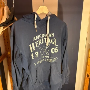 Blå hoodie från Solid med tryck - Snygg marinblå hoodie från Solid med vit text och tryck framtill. Tröjan har huva med grå insida och vita snören, samt en stor magficka. Perfekt för dig som gillar en avslappnad och cool stil.