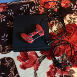 PlayStation4  - Bilderna visar en spelkonsol (PlayStation 4) med en röd handkontroll och tillhörande kablar. Perfekt för dig som vill spela med vänner eller online. Allt du behöver för att komma igång med gaming direkt! 