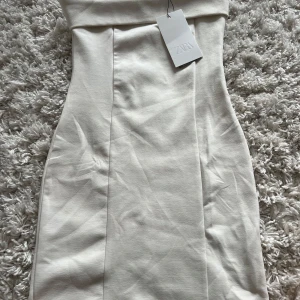 Vit axelbandslös kortklänning Zara - Snygg vit axelbandslös kortklänning från Zara med figurnära passform. Klänningen har stilrena sömmar framtill och en enkel, elegant design som passar perfekt till sommarens alla tillfällen.