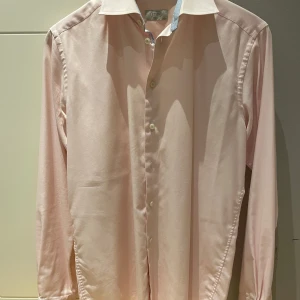 Ljusrosa skjorta från Eton, slim fit 40 - Snygg ljusrosa skjorta från Eton i slim fit-modell. Skjortan har klassisk krage, vita knappar och diskreta rutiga detaljer i blått på insidan av kragen och knappslån. Perfekt för dig som gillar stilrena plagg med en twist.