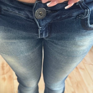 Blå bootcut jeans från Colcci - Snygga blå jeans från Colcci med bootcut passform. Jeansen har klassisk femficksdesign, dragkedja och knapp framtill samt Colcci Denim-märke på bakfickan. Materialet är mjukt jeans och färgen är mörkblå med ljusare tvättade partier.