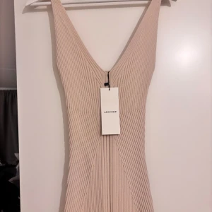  Adoore klänning  - Supersnygg stickad långklänning från Adoore i cremevit nyans. Klänningen har djup v-ringning, ribbad struktur och är ärmlös. Perfekt för dig som gillar en stilren och modern look med en figurnära passform.