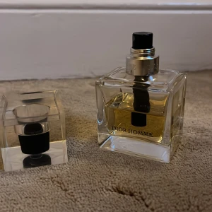 Dior Homme parfym 100ml - Dior Homme parfym i en stilren, fyrkantig glasflaska med svart och silverfärgad spraydel. Flaskan har tydlig Dior Homme-text och innehållet är gyllengult. Snygg och modern design som känns lyxig och tidlös.