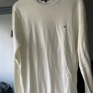 Vit bomullströja Tommy Hilfiger M - Klassisk vit långärmad tröja från Tommy Hilfiger i mjuk bomull. Tröjan har rund halsringning med diskret röd och marinblå rand på insidan samt liten broderad logga på bröstet. Perfekt för en clean och stilren look.