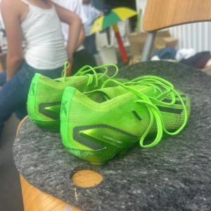 Adidas gröna fotbollsskor X Speedportal - Säljer ett par Adidas X Speedportal fotbollsskor i neon-grönt med svarta detaljer och klassiska tre ränder på sidan. Skorna har snörning och är tillverkade i syntetmaterial för lätt känsla och bra grepp på planen. Perfekta för dig som vill sticka ut på fotbollsplanen.