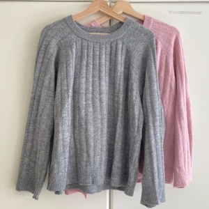 Ribbstickad tröja i grått och rosa - Två mysiga ribbstickade tröjor i grått och ljusrosa. Båda har rund hals, lång ärm och breda ribbade muddar vid ärmslut och nederkant. Perfekt för dig som gillar enkel stil med lite struktur. Materialet känns mjukt och värmande, passar skönt under höst och vinter. 2 för 100kr eller 1 för 70kr