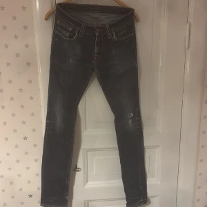 Mörkblå  jeans från Nudie Jeans - Snygga blåa jeans från Nudie Jeans med snygga slitningar och klassiska orangea sömmar på bakfickorna. Modellen har fem fickor, smal passform och är tillverkad i stretchigt jeanstyg.