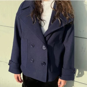 Design by si kappa  - Snygg mörkblå skepparkavaj med dubbelknäppning och stora slag. Jackan har breda ärmslut med knappdetaljer och två fickor framtill. Tillverkad i ett mjukt ull-liknande material som känns lyxigt och passar perfekt till kyliga dagar.