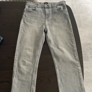 Grå jeans från Lee, raka ben - Snygga grå jeans från Lee med klassisk femficksdesign och raka ben. Jeansen har en ljusgrå tvätt och är tillverkade i mjukt bomullstyg. Perfekta för dig som gillar en clean och stilren look.