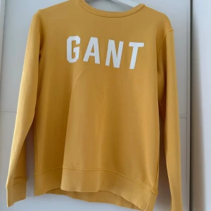 GANT tröja - Gul sweatshirt från GANT med stor vit logga framtill. Tröjan har rund halsringning och långa ärmar. Tillverkad i mjuk bomull som känns skön mot huden. Nästan helt oanvänd!!