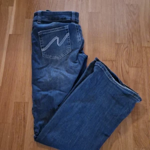 Blå bootcut jeans från Nelly - Snygga blå jeans från Nelly med bootcut passform och klassisk femficksdesign. Jeansen har låg midja och coola broderade detaljer på bakfickorna. Perfekta för dig som gillar en avslappnad och trendig stil. Materialet är klassisk jeans i bomull.