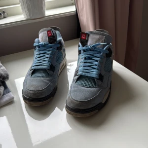 Nike Air Jordan 4 University Blue - Säljer ett par Nike Air Jordan 4 University Blue sneakers med ljusblå mocka, svarta och vita detaljer samt meshpaneler. Skorna har snörning, synlig Air-sula och coola 23-detaljer på plösen. Perfekta för dig som vill sticka ut med en ikonisk och sportig look.