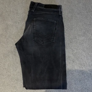 Replay Anbass svarta jeans - Snygga svarta Replay Anbass jeans med diskret tvättad look. Klassisk femficksmodell med svarta sömmar och Replay-logga på bakfickan. Jeansen har normal passform och är tillverkade i mjukt jeansmaterial med stretch för extra komfort.