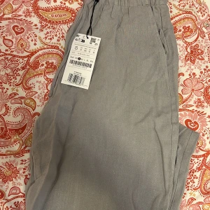 Ljusgrå linnebyxor med snörning - Säljer ett par ljusgrå linnebyxor i storlek S. Byxorna har elastisk midja med snörning och raka, lite loose ben. Perfekta för chill dagar eller när du vill ha en avslappnad stil. Tillverkade i 100% linne för en luftig känsla.