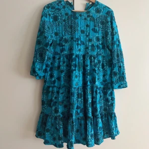 Blå blommig kortklänning med volang - Supersöt blå kortklänning med blommigt mönster och volangdetaljer. Klänningen har rund hals, trekvartsärm och en luftig passform som ger en skön och avslappnad vibe🙏🏻🤝