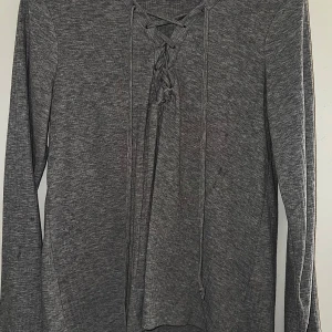 Grå långärmad tröja med snörning BikBok - Grå långärmad tröja från BikBok med snygg snörning framtill vid halsen. Tröjan är i mjukt material med en ribbad look och har en relaxed passform. Perfekt för dig som gillar stilrena basplagg.