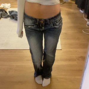 Lågmidjade blå jeans med bootcut - Säljer ett par blå jeans med låg midja och bootcut. Jeansen har slitna detaljer och råa kanter nertill. 