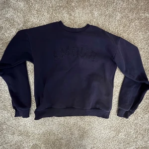 Mörkblå sweatshirt från Gina Tricot - Mörkblå sweatshirt från Gina Tricot med texten 'AMOUR' i svarta pärlor framtill. Tröjan har rund hals, ribbade muddar och är långärmad. Perfekt för dig som gillar en enkel men ändå snygg look.