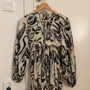 Plisserad svartvit långklänning - Säljer en plisserad långklänning i svartvitt mönster med v-ringning och långa ärmar. Klänningen har ett coolt abstrakt mönster och resår vid ärmsluten. Perfekt för dig som gillar statement-plagg med flowy känsla.