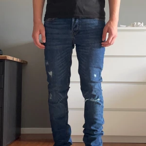 Jack & Jones Slim Straight Tim Jeans - Snygga blå jeans från Jack & Jones, modell Tim Slim Straight. De har en klassisk femficksdesign, regular rise och smal passform genom lår och knä. Jeansen är i denim med slitna detaljer framtill för en cool look. Perfekta till sneakers och hoodie. Nya med lappar.