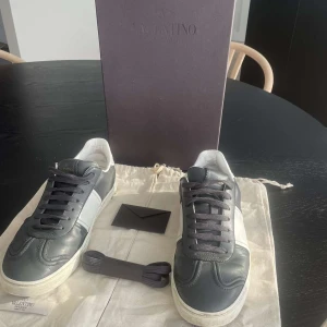 Valentino fly crews - Snygga sneakers från Valentino Garavani i mörkgrått och vitt skinn. Klassisk rund tå, mörkblå snören och coola nitar baktill på sulan. Sulan har ett unikt mönster och skorna har diskret logga på plösen. Perfekta för dig som gillar exklusiva detaljer. Säljs inte längre!