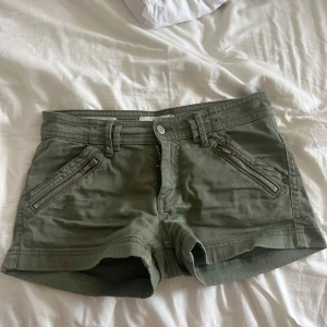 lågmidjade jeansshorts - Snygga olivgröna shorts med två dragkedjor framtill och klassiska bakfickor. Perfekta för varma dagar och ger en cool vibe till din outfit.