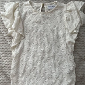 Vit blus med volangärmar Holly & White - Supersöt vit blus från Holly & White med strukturmönster och volangiga korta ärmar. Blusen har rund halsringning och knäppning bak i nacken. Nästan inte använd! 