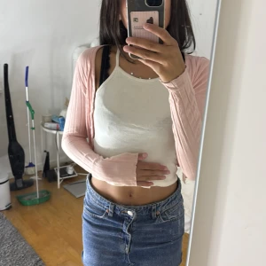 Croppad rosa kofta från SHEIN XS - Söt croppad kofta från SHEIN i ljusrosa med ribbad struktur och långa ärmar. Koftan har knappar framtill och är i ett mjukt, stretchigt material som känns lätt på kroppen. Perfekt att slänga över ett linne för en chill look.