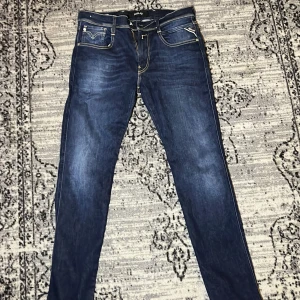 Replay Anbass slim jeans blå, stl 32 - Snygga mörkblå Replay Anbass jeans i slim fit med klassiska kontrastsömmar och fem fickor. Jeansen är tillverkade i återvunnet denim och har en stilren look med raka ben och diskreta slitningar. Perfekta för dig som gillar en modern och clean stil.