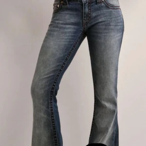 Blå bootcut jeans med kontrastsömmar - Snygga blå jeans med bootcut-modell och markerade kontrastsömmar. Jeansen har klassiska bakfickor med dekorativa sömmar och en lätt tvättad look. Perfekta för dig som gillar en retrovibe och vill ha ett par jeans som sticker ut.