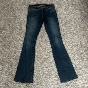 Bootcut jeans från American Eagle - Mörkblå bootcut jeans från American Eagle Outfitters med snygga slitningar och kontrastsömmar. Modellen är super stretch för extra bekvämlighet och har klassiska fem fickor samt broderad detalj på bakfickorna. Jensen är i jättebra skick utom en av kanterna (bild) som går att fixa lätt