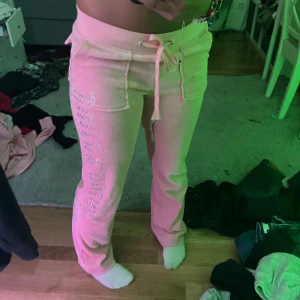 Rosa Juicy Couture mjukisbyxor - Säljer ett par ikoniska rosa mjukisbyxor från Juicy Couture i mjuk velour. Byxorna har snörning i midjan, stora fickor fram och bak samt glittrig Juicy Couture-text längs benet. Står storlek M men passar mer som small.