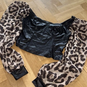 Svart korsettopp med leopardärmar Shein - Cool svart korsettopp från Shein med glansig skinnlook och ballongärmar i leopardmönster. Toppen är croppad och har breda muddar i svart skinnimitation vid ärmsluten. Perfekt statement-piece för dig som vill sticka ut.