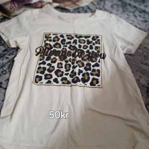 Vit t-shirt med leopardmönster - Snygg vit t-shirt med ett stort leopardmönstrat tryck framtill och texten 'Always be you' över motivet. Klassisk rund halsringning och korta ärmar. Perfekt för dig som vill sticka ut med coola detaljer och djurmönster.