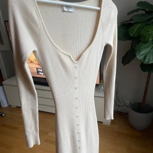 Beige ribbad långklänning Chiquelle - Mjuk ribbad långklänning från Chiquelle i beige. Klänningen har lång ärm, v-ringning, knappar framtill och en liten slits nertill. Figurnära passform men med skön stretch. Använd en gång.