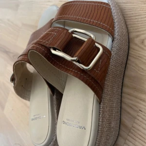 Bruna Vagabond sandaler med spänne - Snygga sandaler från Vagabond med breda bruna remmar i skinnlook och stora silvriga spännen. Plattformsula i beige textil ger en cool vibe. Perfekta för sommaren och lätta att matcha till olika outfits.