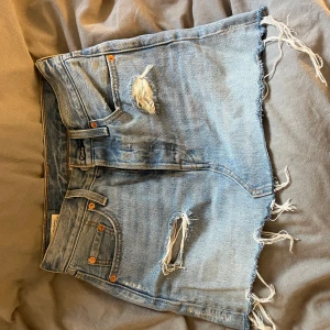 Levi's ljusblå jeanskjol med slitningar - Ljusblå jeanskjol från Levi's med råa, fransiga kanter och slitna detaljer framtill. Klassisk femficksmodell med Levi's-logga bak. Perfekt för en avslappnad och cool stil.