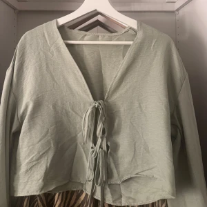 Ljusgrön tröja med knyt - Superfin ljusgrön  tröja med v-ringning och dubbla knyt framtill. Långärmad och i ett tunt, mjukt bomullstyg som känns luftigt och skönt. Perfekt att styla över ett linne eller klänning för en chill look.