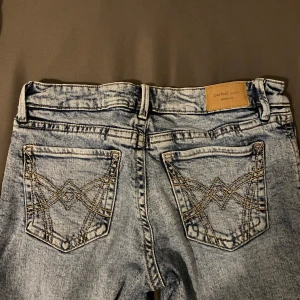 Ljusblå Perfect Jeans med broderade fickor - Säljer ett par ljusblå jeans från Gina Tricot, modellen Perfect Jeans. De har ett litet hål längst ner, men syns knappt när man väl har byxorna på. Använd ett fåtal gånger.