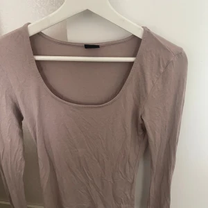 Beige långärmad topp med rund hals - En enkel och stilren beige långärmad topp med rundad, djup ringning. Perfekt att matcha med jeans eller kjol för en clean look. Mjuk och skön i bomullsmaterial, passar året runt.