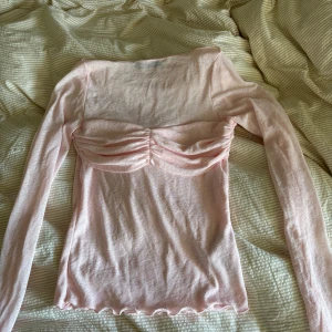 Ljusrosa långärmad topp med rynk - Supersöt ljusrosa långärmad topp med rynkade detaljer över bysten och vågig kant nertill. Tunn och mjuk i materialet, perfekt för dig som gillar romantisk och feminin stil. Sitter figurnära och har en snygg, enkel design som passar till jeans eller kjol.