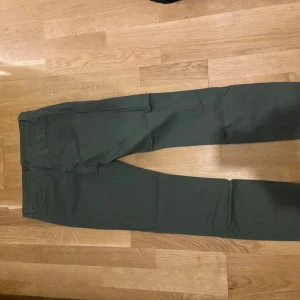 Mörkgröna chinos från lager 157, storlek M - Snygga mörkgröna chinos från lager 157  i storlek M. Byxorna har raka ben, bälteshällor och klassiska bakfickor. Tillverkade i mjuk bomull med dragkedja och knapp framtill. Perfekta för en clean och stilren look.
