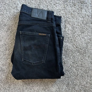 Mörkblå jeans från Nudie Jeans - Snygga mörkblå jeans från Nudie Jeans med klassisk femficksdesign och subtila slitningar. Jeansen har raka ben, knappgylf och diskret logga på bakfickan. Perfekta för dig som gillar stilrena och tidlösa jeans med bra passform.