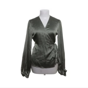 Grön omlottblus i satin - Snygg olivgrön omlottblus i glansigt satinmaterial med långa ärmar och knyt i sidan. Perfekt för dig som gillar en elegant och trendig look med lite extra lyxig känsla.